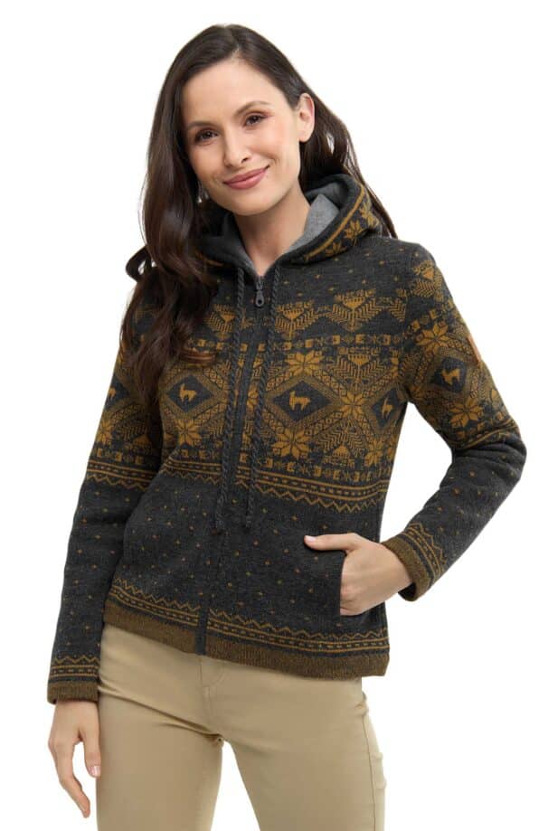 Eine lächelnde Frau trägt eine gemusterte Kapuzenjacke in Dunkelgrau und Gelb mit Reißverschluss, die Hände in den Taschen.