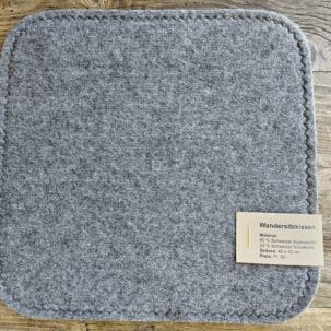 Graues Wandersitzkissen aus Filz mit einer Preistafel auf einem Holztisch.